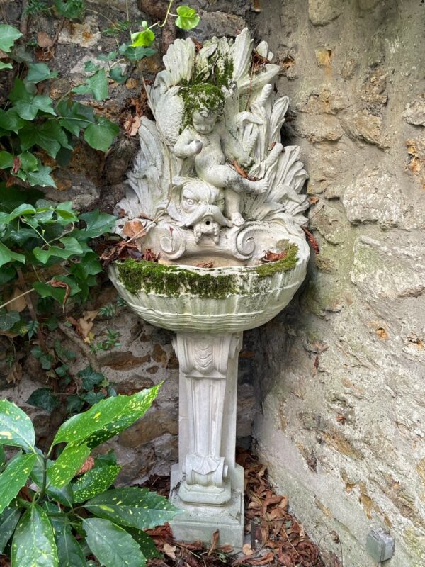 Jolie fontaine d’extérieur en pierre reconstituée de style Louis XV a décors d’un enfant reposant sur une tète de triton